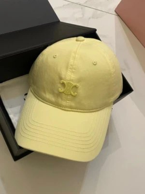 Ljusgul keps från Celine - Snygg ljusgul keps från Celine med det ikoniska Triomphe-emblemet broderat framtill. Klassisk böjd skärm och justerbar rem bak. Tillverkad i ett mjukt och lätt material som passar perfekt till en avslappnad streetwear-look.