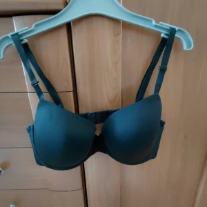 Svart bh, 85C - Stilren svart push-up bh med släta kupor och justerbara axelband. Bh:n har bygel och bredare sidopartier för extra stöd. Passar perfekt under tighta toppar tack vare den sömlösa designen. Knappt använda.  