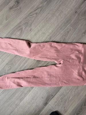 Rosa ribbade leggings från stronger - Säljer ett par snygga rosa träningsleggings med ribbad struktur och hög midja. De är stretchiga och sitter tajt längs benen, perfekta för en avslappnad och trendig look. Passar till både oversized tröjor och crop tops.  Storlek M