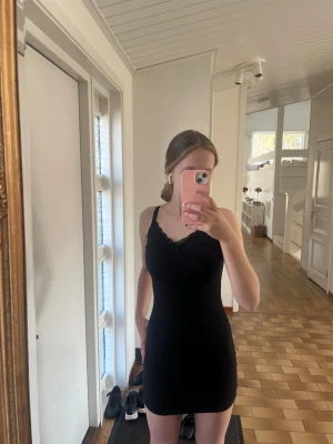 Svart ribbad kort klänning med spets - Säljer en svart, ribbad kort klänning med smala axelband och v-ringning. Klänningen har fina spetsdetaljer vid urringningen och en liten rosett framtill. Köpt på HM, storlek XXS, men stretchig och justerbara axelband. Pris kan diskuteras och skicka om ni har frågor!