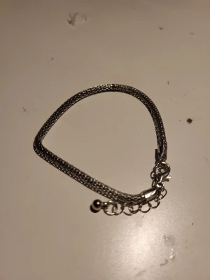 Silvrigt kedjearmband med kula - Snyggt armband i silverfärgad metall med dubbla kedjor och en liten rund kula vid förlängningskedjan. Armbandet har ett klassiskt karbinlås och justerbar längd för perfekt passform. Perfekt accessoar för att lyfta din stil.