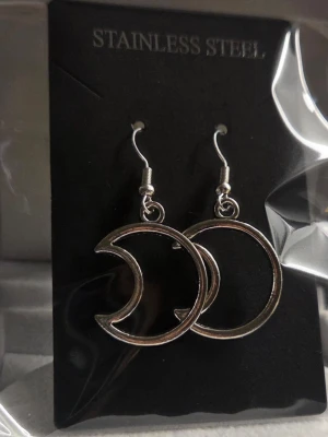 Silvriga örhängen i månform - Snygga örhängen i rostfritt stål med en cool, öppen månformad design. De är silvriga och har krokar för enkel användning. Perfekta för dig som gillar unika accessoarer med en modern touch. Ca 2,5 cm.