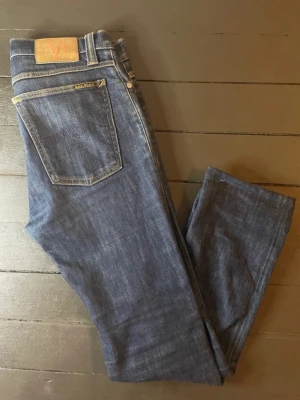 Blå Nudie Jeans High Kai - strl 31/34 - Säljer dessa blåa Nudie byxor av modell High Kai i storlek 31/34. Notera dock att byxorna är avklippa samt uppsydda så längden stämmer inte riktigt. Det är inget större slitage på byxorna. Innerbenslängden är 70cm. Benöppningen är 32cm i omkrets och midjan är 84cm i omkrets. Priset kan diskuteras. Hör av er vid frågor. 