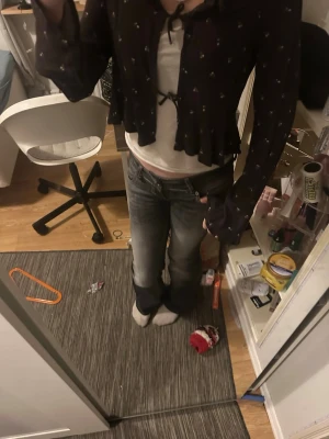 Mörkblommig blus från H&M - Söt mörkblommig blus från H&M med små vita blommor, knytband framtill och volangkant nedtill. Blusen har långa ärmar och är gjord i ett tunt, luftigt material som ger en avslappnad och trendig look.