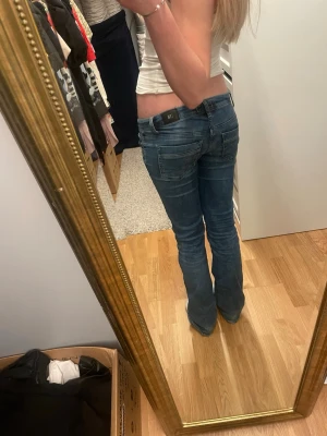 Blå bootcut jeans från LTB - Säljer ett par blå bootcut jeans från LTB med låg midja och klassiska fem fickor. Jeansen har en snygg tvätt och sitter tajt över låren för att sedan bli vidare nedtill. Perfekta till en avslappnad och trendig look.