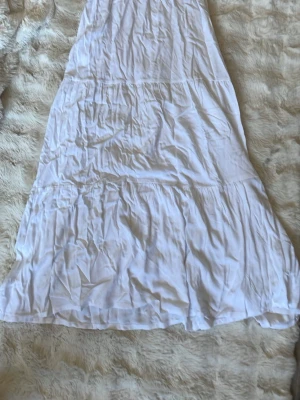 Vit långklänning från 157 XS - Luftig vit långklänning från 157 i storlek XS. Klänningen har flera volangliknande sömmar och är tillverkad i ett tunt, mjukt tyg som känns perfekt för varma dagar. Enkel och stilren design som passar till många tillfällen. Pris 30kr