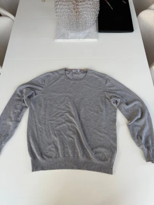 Ljusgrå stickad tröja Gran Sasso - Snygg ljusgrå stickad tröja från Gran Sasso i mjuk bomull. Tröjan har rund halsringning, långa ärmar och ribbade muddar vid ärmslut och nederkant. Perfekt för en clean och stilren look.