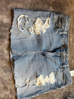 Jeanskjol - Säljer en par ljusblå jeankjol från Hollister med råa, fransiga kanter. Kjolen har stora slitningar framtill för en trendig look och klassiska fickor både fram och bak. Perfekta för sommaren! Passar 36