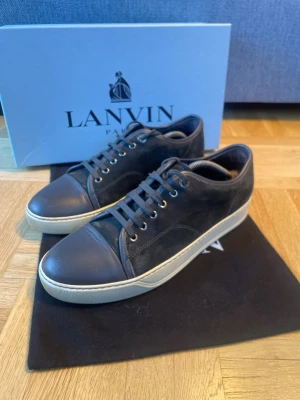 Svarta Lanvins - Snygga svarta sneakers från Lanvin i mocka med matchande svarta skosnören. Snören finns extra. Skorna är i mycket bra skick förutom några små repor på tåboxen som syns på bild 4. Skorna är i storlek UK 8 som motsvarar ungefär 42-43. Kan skicka fler bilder om det skulle behövas.