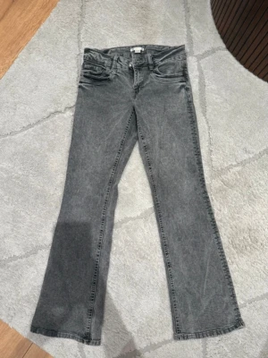 Grå bootcut jeans i tvättad denim - Säljer ett par grå bootcut jeans i tvättad denim med klassisk femficksmodell och normal midja. Jeansen har en lätt utsvängd passform nedtill och är perfekta för en avslappnad men trendig look. Inget synligt märke på bilderna.