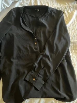 Svart henley-skjorta i bomull - Snygg svart henley-skjorta med lång ärm och knappar framtill. Tillverkad i mjuk bomull och har en avslappnad passform. Perfekt för dig som gillar en enkel men stilren look.