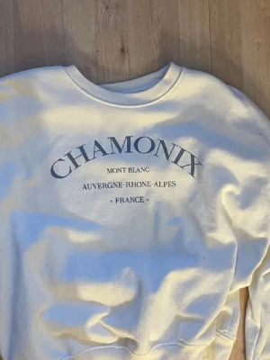 Vit sweatshirt med Chamonix-tryck - Cool vit sweatshirt med tryck 'CHAMONIX Mont Blanc Auvergne-Rhone-Alpes France' på bröstet. Rund halsringning och avslappnad passform, perfekt för en chill look. Materialet är mjukt och bekvämt.