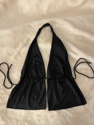Svart topp med knyt - Snygg svart topp i trekantsmodell med knyt i nacken och ryggen. Materialet känns mjukt och följsamt. Enkel och stilren design som passar till allt. Har tyvärr klippt av lappen.
