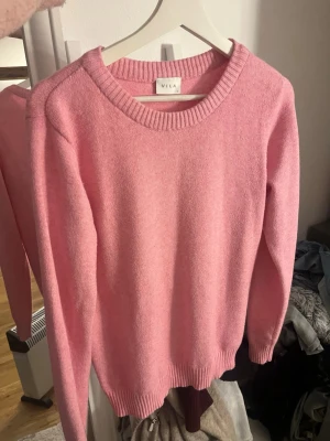 Rosa stickad tröja från Vila - Snygg rosa stickad tröja från Vila med rund halsringning och ribbade muddar vid ärmslut och nederkant. Perfekt för dig som vill ha en enkel men färgglad tröja i garderoben. Passar till både jeans och kjol.