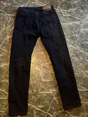 Svarta Disel Jeans - Snygga svarta jeans från Diesel med raka ben och klassisk femficksdesign. Jeansen har en läderpatch med Diesel-logga bak i midjan och diskret röd detalj på ena bakfickan. Tillverkade i mjukt denimtyg som sitter skönt.