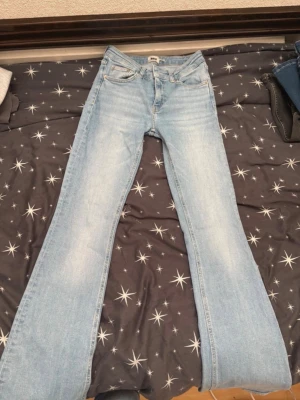 Ljusblå bootcut jeans - Säljer ett par ljusblå bootcut jeans med klassisk femficksdesign och normal midja. Jeansen har en snygg tvätt och vida ben som ger en retrovibe. Perfekta för dig som gillar en avslappnad men trendig stil. Materialet är denim i bomull.