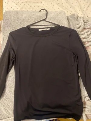 Svart långärmad topp från H&M - En enkel svart långärmad topp från H&M med rund halsringning. Tillverkad i ett mjukt och stretchigt material som känns bekvämt mot huden. Perfekt att styla med jeans eller kjol för en clean look.