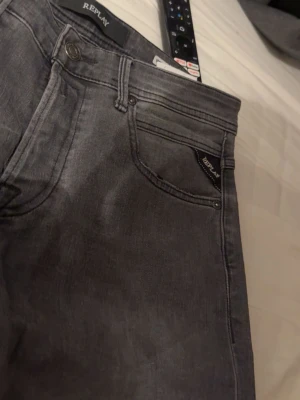 Grå jeans från Replay - Snygga grå jeans från Replay med klassisk femficksmodell och diskret logga på myntfickan. Jeansen har raka ben och är tillverkade i mjukt denimtyg som ger en skön passform. Perfekta för dig som gillar en stilren och avslappnad look.
