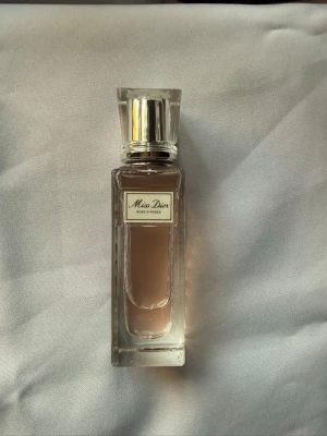 Miss Dior Rose N'Roses parfym -  En lite använd Miss Dior Rose N'Roses parfym i en elegant, rektangulär glasflaska med silverfärgad kork. Doften har en ljusrosa ton och flaskan har en stilren etikett framtill. Perfekt för dig som gillar fräscha och blommiga dofter.
