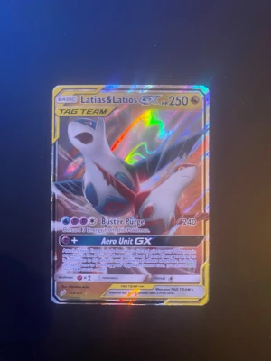 Latias & Latios GX Pokémonkort - Latias & Latios GX TAG TEAM Pokémonkort med holografisk yta. Kortet har färgerna vit, blå, röd och guld samt detaljer i silver. Perfekt för samlare eller Pokémonfans som vill utöka sin samling med ett unikt och glittrigt kort.