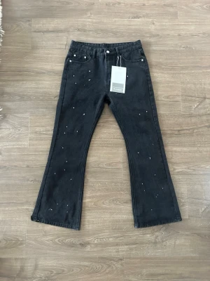 Svarta bootcut jeans med stänk - Ett par svarta bootcut jeans med vita färgstänk för en cool och trendig look. Jeansen har klassisk femficksmodell, hög midja och utsvängda ben. Perfekta för dig som vill ha en edgy stil.😊 Står storlek L i byxan men sitter mer som M.