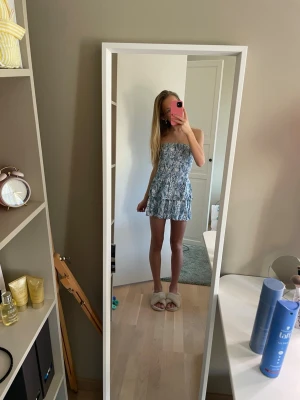 Blåvit axelbandslös kortklänning - Säljer en söt blåvit kortklänning med blommigt mönster och volangdetaljer. Klänningen är axelbandslös of shoulder och den ger en bekväm och snygg passform. Perfekt för varma dagar och sommarens alla tillfällen. Den är i väldigt bra skick använd fåtal gånger . Pris går att diskutera och skriv om ni har frågor!  💓💗