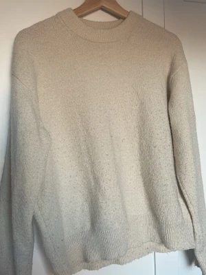 Beige stickad tröja från Gina Tricot - Mysig beige stickad tröja från Gina Tricot med rund halsringning och ribbade muddar vid ärmslut och nederkant. Tröjan har en enkel och stilren design som passar perfekt till lager på lager och är gjord i mjukt material.