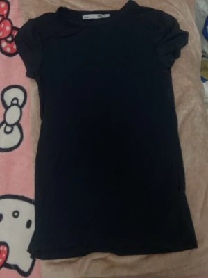 Svart basic t-shirt från H&M - En enkel svart t-shirt från H&M med rund hals och korta ärmar. T-shirten har en klassisk passform och är tillverkad i mjuk bomull, perfekt till alla tillfällen. Stilren och lätt att matcha med olika outfits. Fläck visas i bild