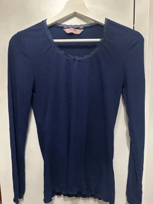 Mörkblå ribbad topp från Hunkemöller - Mörkblå långärmad topp från Hunkemöller med ribbad struktur och spetsdetalj vid halsringningen. Klassisk rund hals och figurnära passform, perfekt att styla till jeans eller kjol.
