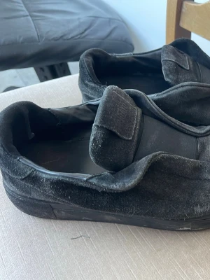 Svarta sneakers från Axel Arigato - Säljer ett par svarta sneakers från Axel Arigato i mocka med kardborreband. Skorna har en låg profil och klassisk siluett med svart yttersula och diskret logga under sulan. Perfekta för en clean och stilren look. Mockan är lite sliten och dem är vattenskadade. Frågor och funderingar skriv priset kan gå ner 