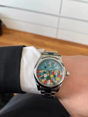 Färgglad klocka  - Unik klocka med färgglad urtavla i blått, rött, gult och vitt. Klockan har ett coolt, lekfullt mönster och ett robust armband i silverfärgad metall. Perfekt för dig som vill sticka ut med din stil. Ge gärna bud 