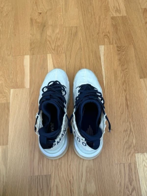 Vita och marinblå basket sneakers - Snygga basket sneakers från Jordan i vitt med marinblå detaljer och snörning. Skorna har högt skaft och textdetaljer på hälen. Ovandelen är i mesh-liknande material för bra andningsförmåga och sulan är ljus med bra grepp.