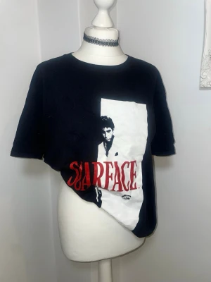 Scarface svart t-shirt med tryck - Cool svart t-shirt med stort Scarface-tryck framtill i vitt och rött. Oversized passform (om du är S-M) och klassisk rund halsringning. Perfekt för dig som gillar film och streetstyle. Har knappt använt. 100% bomull 