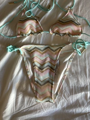 Pastellfärgad missoni mönsterliknande bikini med knyt - Säljer en snygg trekantsbikini med pastellfärgade ränder i mintgrönt, rosa, beige och guld. 