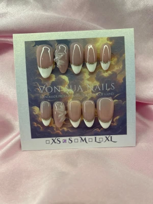 SoftGold (S);Medium Almond - Handgjorda press-on naglar i storlek S: 15 mm, 11,5 mm, 12 mm, 11 mm, 9 mm . Naglarna har en nude bas med vit fransk tipp och tunna gulddetaljer. Några naglar har vita 3D-blommor för extra stil. Perfekt för dig som vill ha en elegant och trendig look.