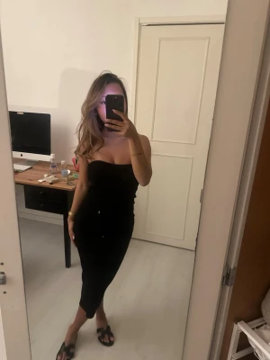 Svart axelbandslös långklänning - Snygg svart axelbandslös långklänning med figurnära passform. Klänningen har en stilren och enkel design som framhäver siluetten. Perfekt för dig som gillar minimalistisk stil och vill ha en klänning som känns både trendig och tidlös.