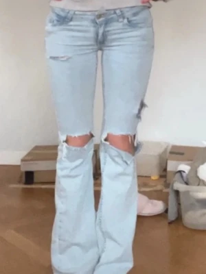 Ljusblå slitna bootcut jeans - Säljer ett par ljusblå bootcut jeans med stora slitningar över knäna från Nelly 