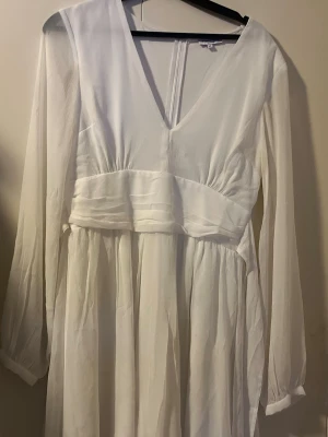 Två vita långklänningar med spets - Säljer två vita långklänningar. Ena har v-ringning, långa ärmar och ett flowy fall i tunt tyg. Den andra är ärmlös med spets upptill och slät kjol, samt dekorativt märke i midjan. Perfekta för student eller sommarens höjdpunkter!  Bild 1 storlek 36..bild 2 storlek 40