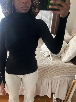 Svart polotröja med knappdetaljer -  en svart, figurnära polotröja med långa ärmar 