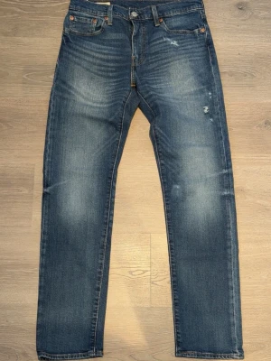 Levi's 502 - Klassiska blå jeans från Levi's med raka ben och lätt slitna detaljer framtill. Jeansen har fem fickor, knappgylf och den ikoniska röda Levi's-lappen bak. Tillverkade i denim med snygg tvätt och subtila slitningar för en avslappnad look. Passar mig som är 180, väger 70 kg