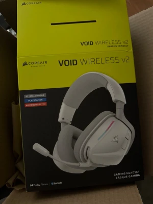 Corsair Void Wireless v2 gaming headset - Trådlöst gamingheadset från Corsair, modell Void Wireless v2. Headsetet är vitt med silverdetaljer och har en justerbar mikrofon. Öronkåporna är vadderade för extra komfort och headsetet har RGB-belysning på sidorna. Kompatibelt med PC, Mac, Playstation och Nintendo Switch. Både via Bluetooth och 2,4ghz USB dongel. Fungerar finfint och är knappt använd. Säljes pga fått ett par andra hörlurar.  Nypris ca 1300kr.