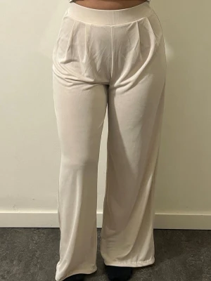 Vida beige kostymbyxor med hög midja - Säljer ett par beige mjukisbyxor med hög midja och vida ben. Byxorna har bred resår i midjan och mjukt, stretchigt material som känns skönt mot huden. Byxorna har två små fläckar men som knappt syns. 