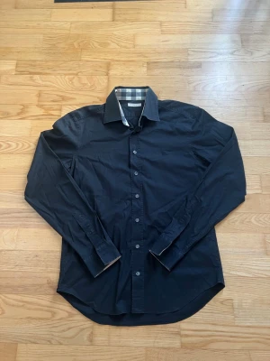 Burberry skjorta svart M - Säljer en fräsch burberry skjorta i färgen svart och storleken M. Skicket på skjortan är dunder. Skjortan är använd en gång på en fest. Måren på skjortan är: Bred - 45cm och längd - ca 110cm. Hör gärna av dig vid frågor. Frakt sker alltid inom 24h!💨📦