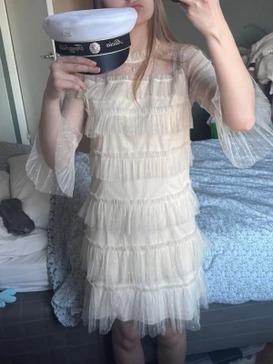 Ljus volangklänning - studentklänning  - Superfin ljus (beige/cremefärgad) kortklänning med flera lager volanger och transparenta ärmar i prickigt tyll. Klänningen har en rak passform och är perfekt för student eller sommarfest. Från Vila 