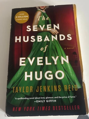 The Seven Husbands of Evelyn Hugo - En engelskspråkig roman med färgstark omslagsdesign, där en kvinna i grön klänning står i centrum. Boken är en New York Times bestseller och utforskar glamour, kärlek och hemligheter i Hollywood. Perfekt för dig som gillar dramatik och gripande berättelser.