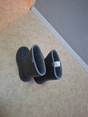 Grå fodrade stövlar från stormberg - Mörkgrå stövlar från Tretorn med mjukt, grått foder och högt skaft. Stövlarna har en enkel design med rund tå och ljusgrå kant upptill. Perfekta för kalla och blöta dagar.