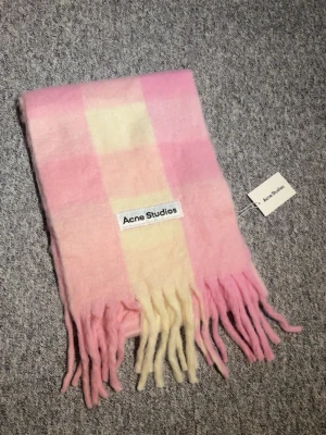 Rutig halsduk från Acne Studios - Supermjuk halsduk från Acne Studios i pastellrosa och ljusgul rutig design. Klassisk rektangulär form med långa fransar i ändarna och tydlig logotyp. Perfekt för att lyfta din outfit med en färgklick. Pris kan diskuteras 😊