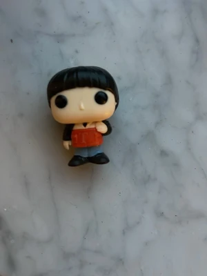 Kinder  figur med svart hår - Rolig Kinder figur med svart pagefrisyr, stora svarta ögon och kläder i svart, rött och blått. Figuren håller i en röd bok och har svarta skor. Perfekt för samlare eller som dekoration.