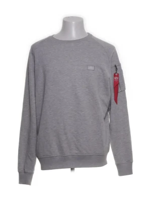 Grå sweatshirt från Alpha Industries - Stilren grå sweatshirt från Alpha Industries med rund halsringning och ribbade muddar. På vänster ärm finns en ficka med dragkedja och den klassiska röda taggen. Perfekt för en avslappnad och trendig look.