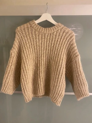 Beige chunky stickad tröja - Säljer en beige chunky stickad tröja med bred ribbstickning och rund hals. Tröjan har en avslappnad passform och lite kortare modell med vida ärmar. Perfekt för lager på lager och riktigt mysig till hösten.